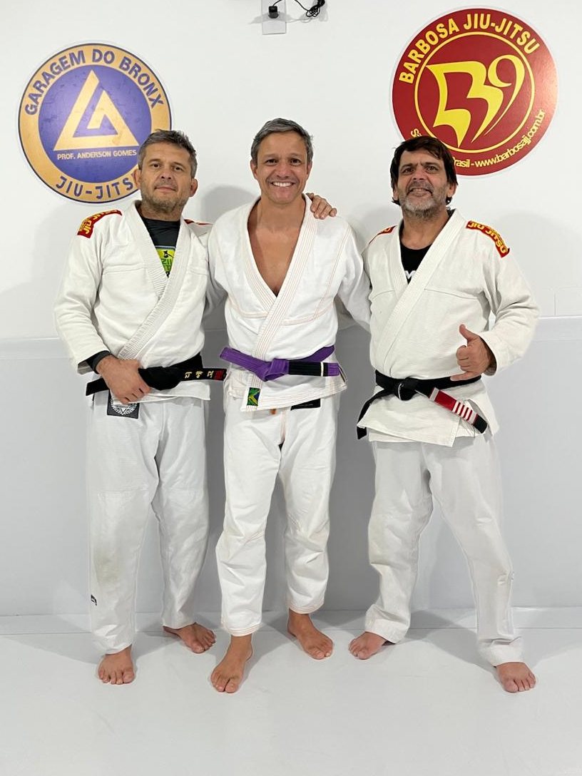Alunos e professores de kimono no tatame do Garagem do Bronx, com as logos do dojo na parede